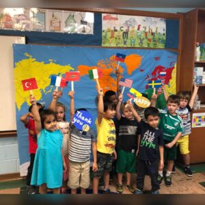Preschoolers showing up their flags in front of a world map during international day at the French American Academy